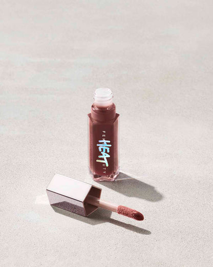 open tube of Fenty Beauty Gloss Bomb Heat Universal Lip Luminizer + Plumper in shade Hot Chocolit Heat with doe foot applicator on concrete background