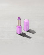 Open product shot of Gloss Bomb Stix Shimmer in shade Ice Amethyst on a concrete background.