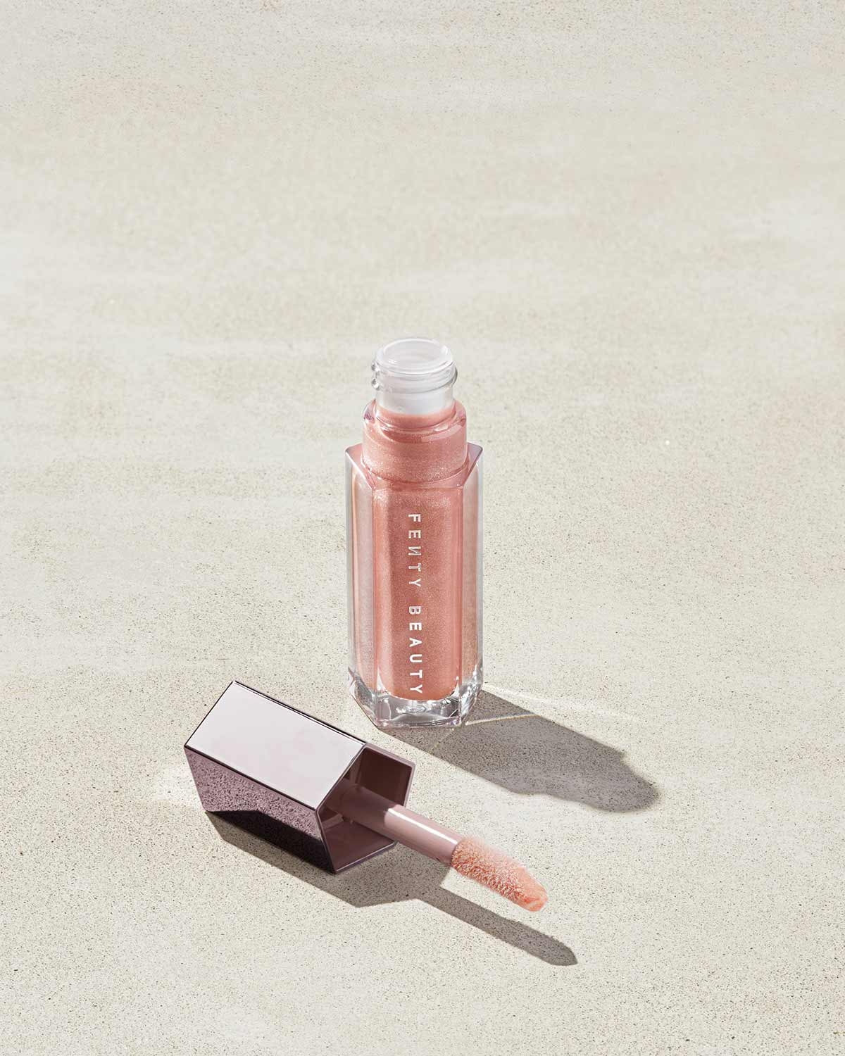 An open tube of Gloss Bomb Universal Lip Luminizer in the shade $weet Mouth on a grey background.