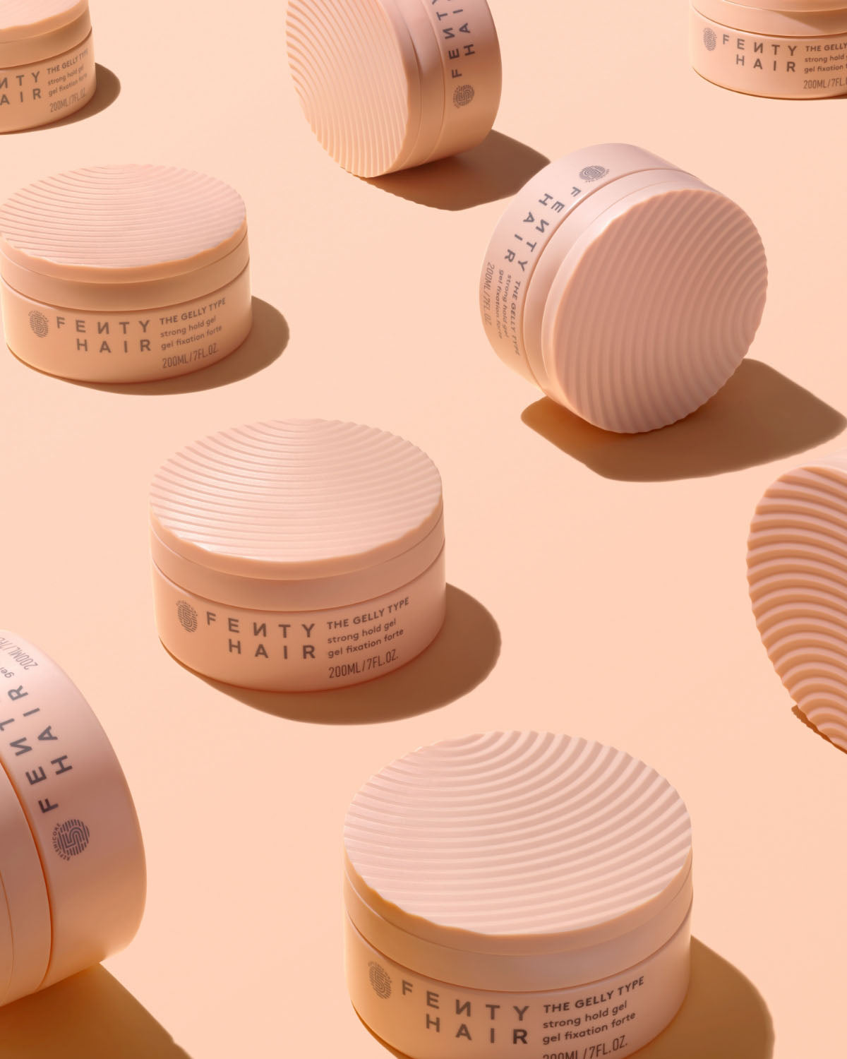 Tubs of Fenty Hair The Gelly Type Strong Hold Gel on a peach colored background.